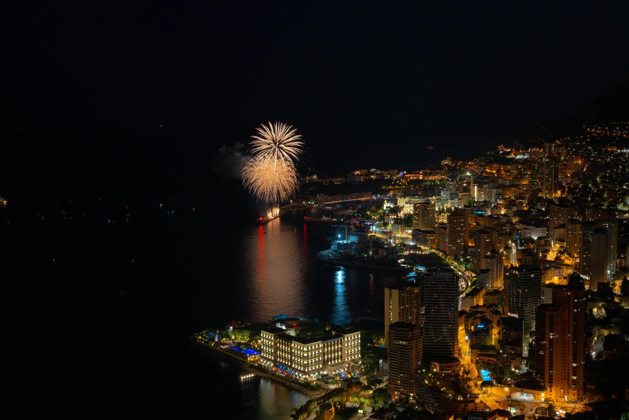 Nighttime Monaco harbour with illuminated city skyline and fireworks bursting over the sea