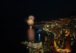Nighttime Monaco harbour with illuminated city skyline and fireworks bursting over the sea
