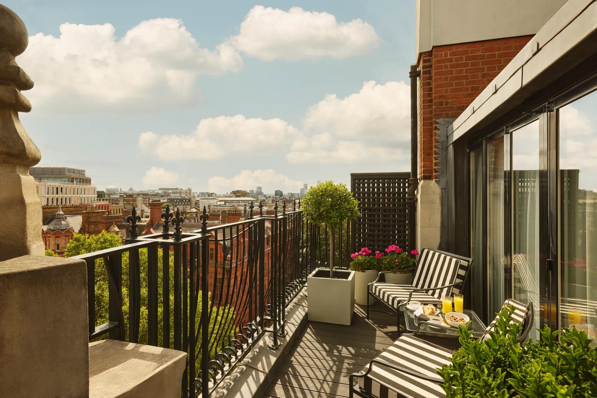 Private balcony with striped loungers, potted plants, and city skyline views under a blue sky.