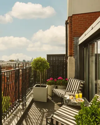 Private balcony with striped loungers, potted plants, and city skyline views under a blue sky.