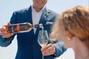 Serveur en costume bleu versant du rosé dans le verre d’une cliente sur une terrasse ensoleillée.