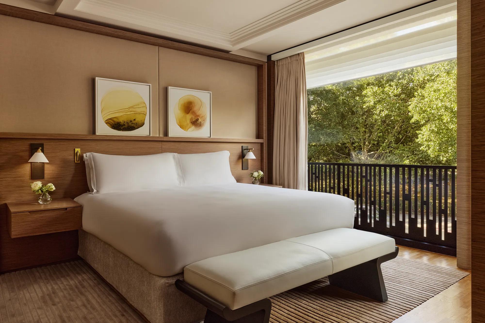 Modern guest room with king bed, upholstered bench, abstract artwork and balcony overlooking lush trees