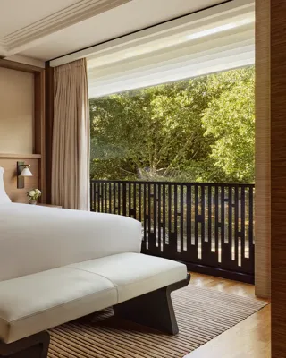 Modern guest room with king bed, upholstered bench, abstract artwork and balcony overlooking lush trees