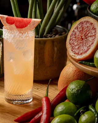 Two citrus cocktails garnished with mint and grapefruit sit among fresh limes, grapefruit and red chillies on a wooden display.