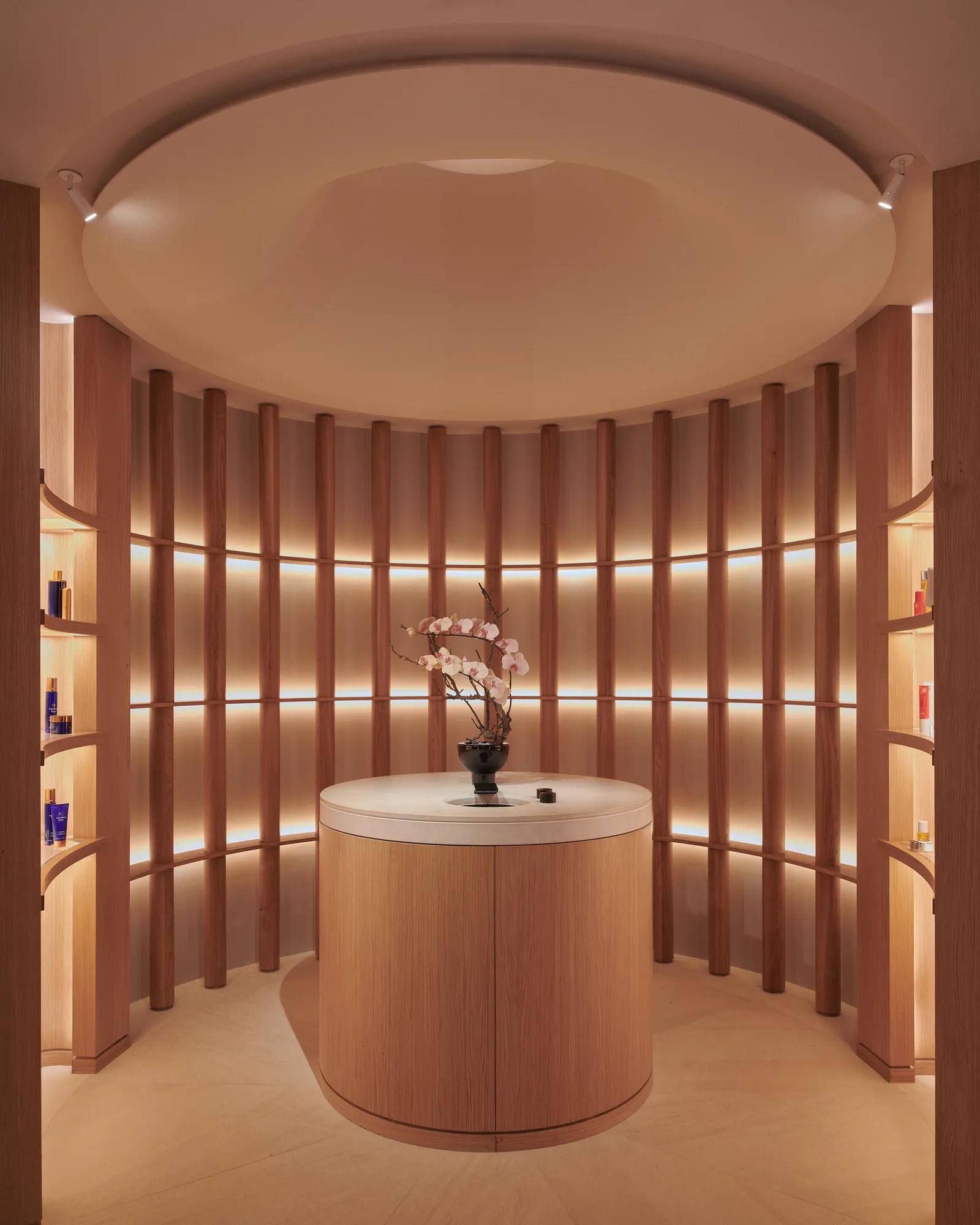 Circular spa retail display with curved wood shelves, softly lit product niches, and a central counter with orchid arrangement beneath a domed ceiling.