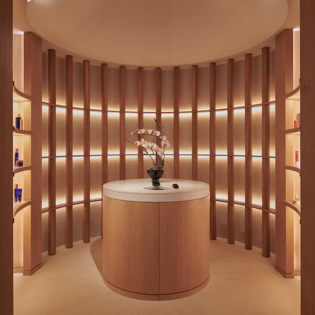 Circular spa retail display with curved wood shelves, softly lit product niches, and a central counter with orchid arrangement beneath a domed ceiling.