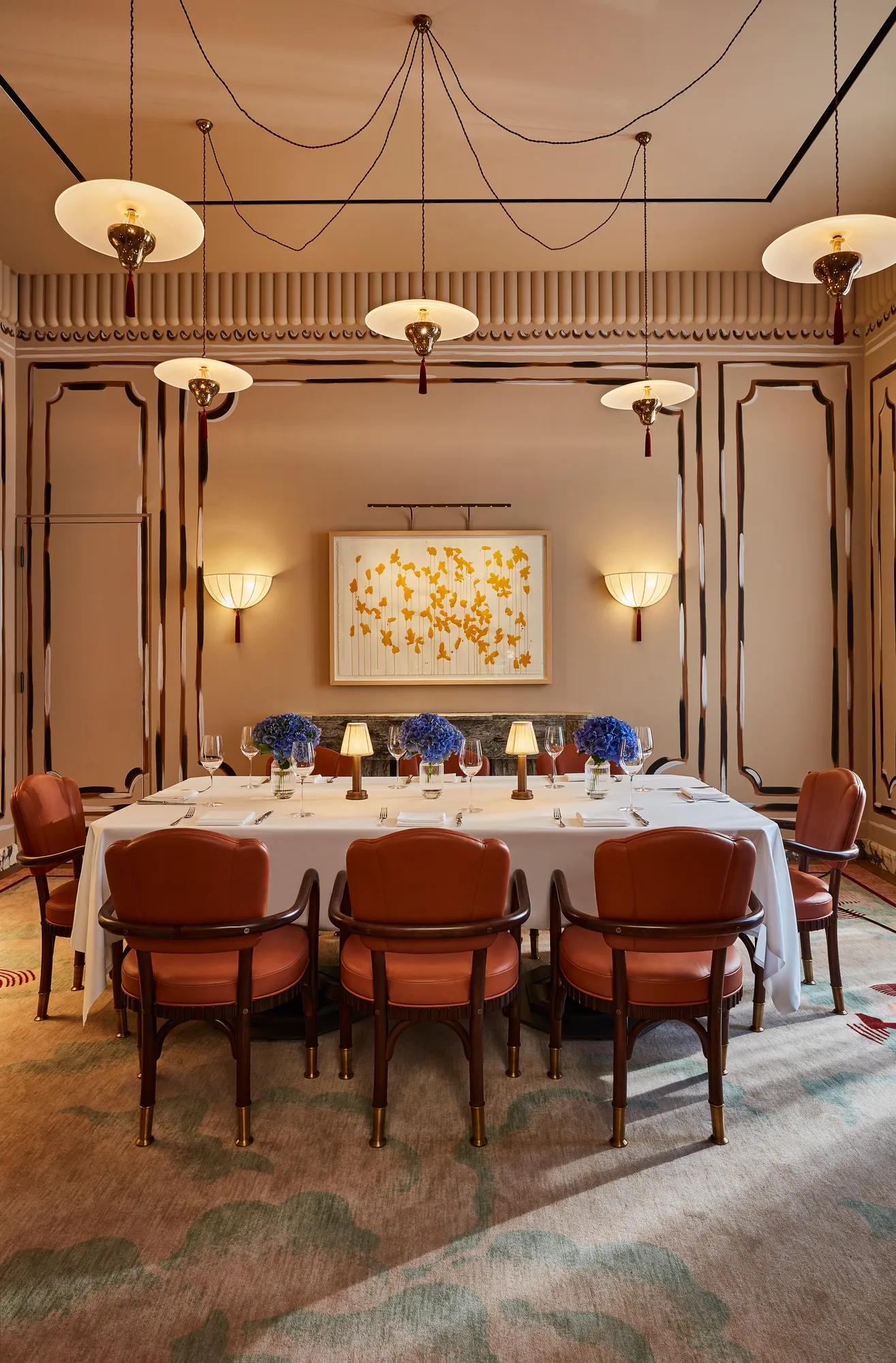 Elegant private dining room with long table, red chairs, blue floral centerpieces, and modern ceiling lights.