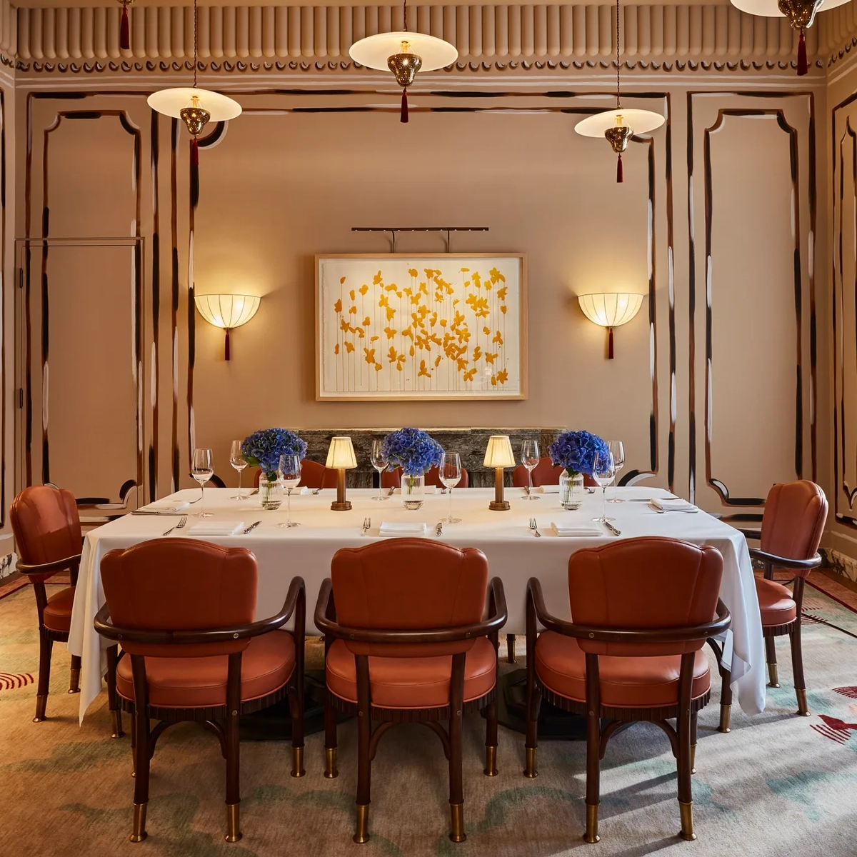 Elegant private dining room with long table, red chairs, blue floral centerpieces, and modern ceiling lights.
