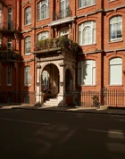 Historic red-brick building with arched stone entrance, floral balcony, and decorative wrought-iron railings.