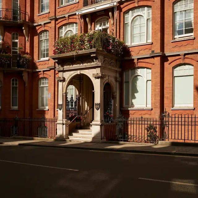 Historic red-brick building with arched stone entrance, floral balcony, and decorative wrought-iron railings.