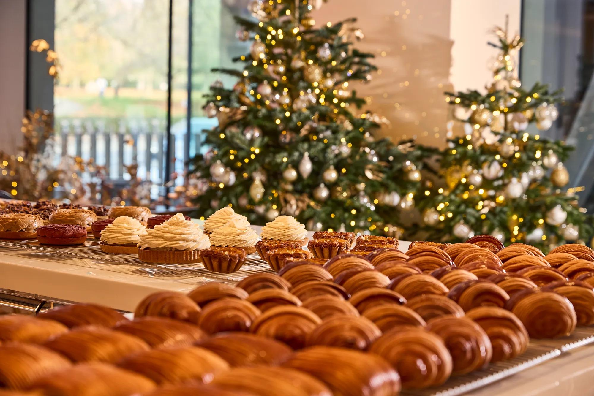 Assorted pastries displayed on a counter with decorated Christmas trees glowing in the background.