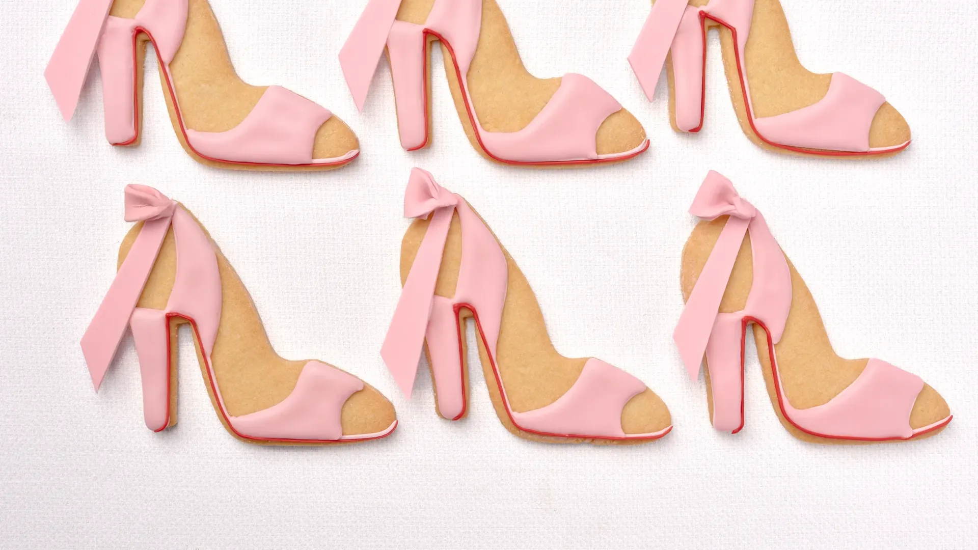 Six pink high-heel cookies with ribbon details arranged on a white background.