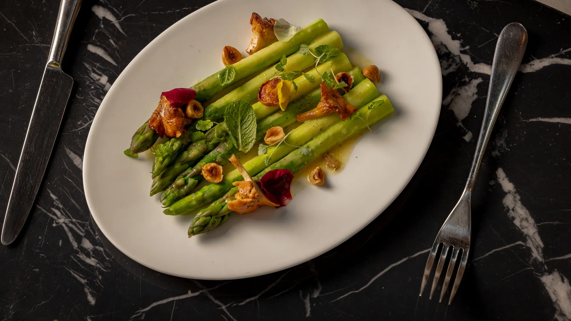 White plate filled with cooked asparagus spears set on a polished black marble countertop.