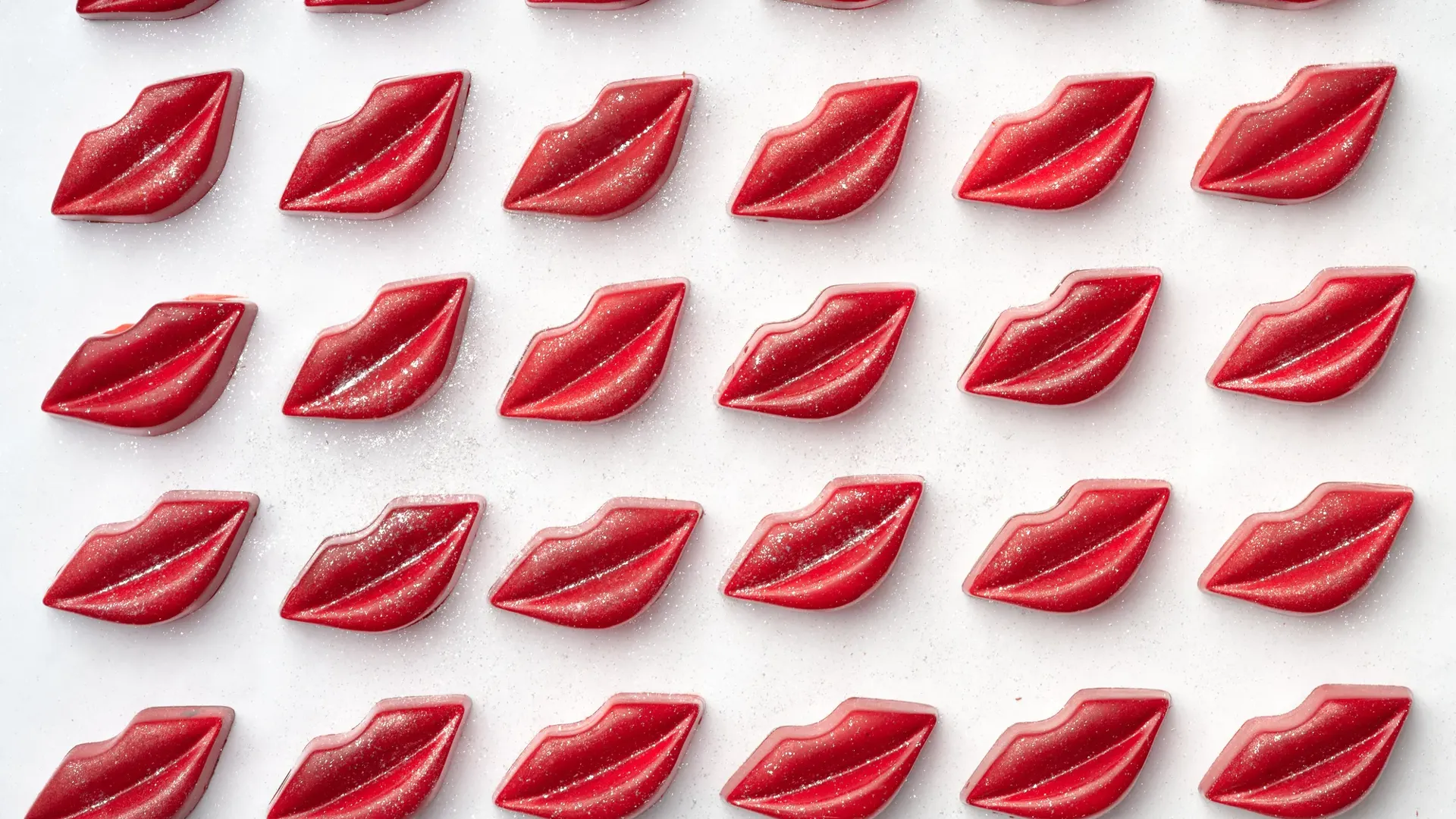 Rows of red lip-shaped chocolates dusted with glitter on a white surface.