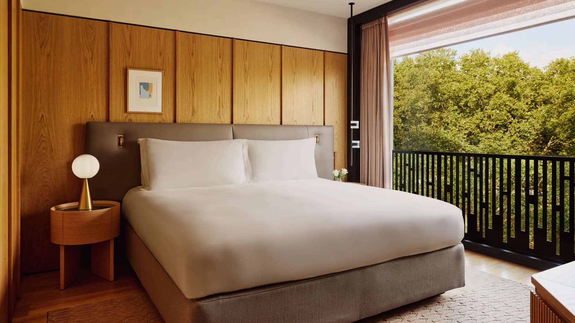 Hotel bedroom with king bed, bedside lamps, and city view through large window.