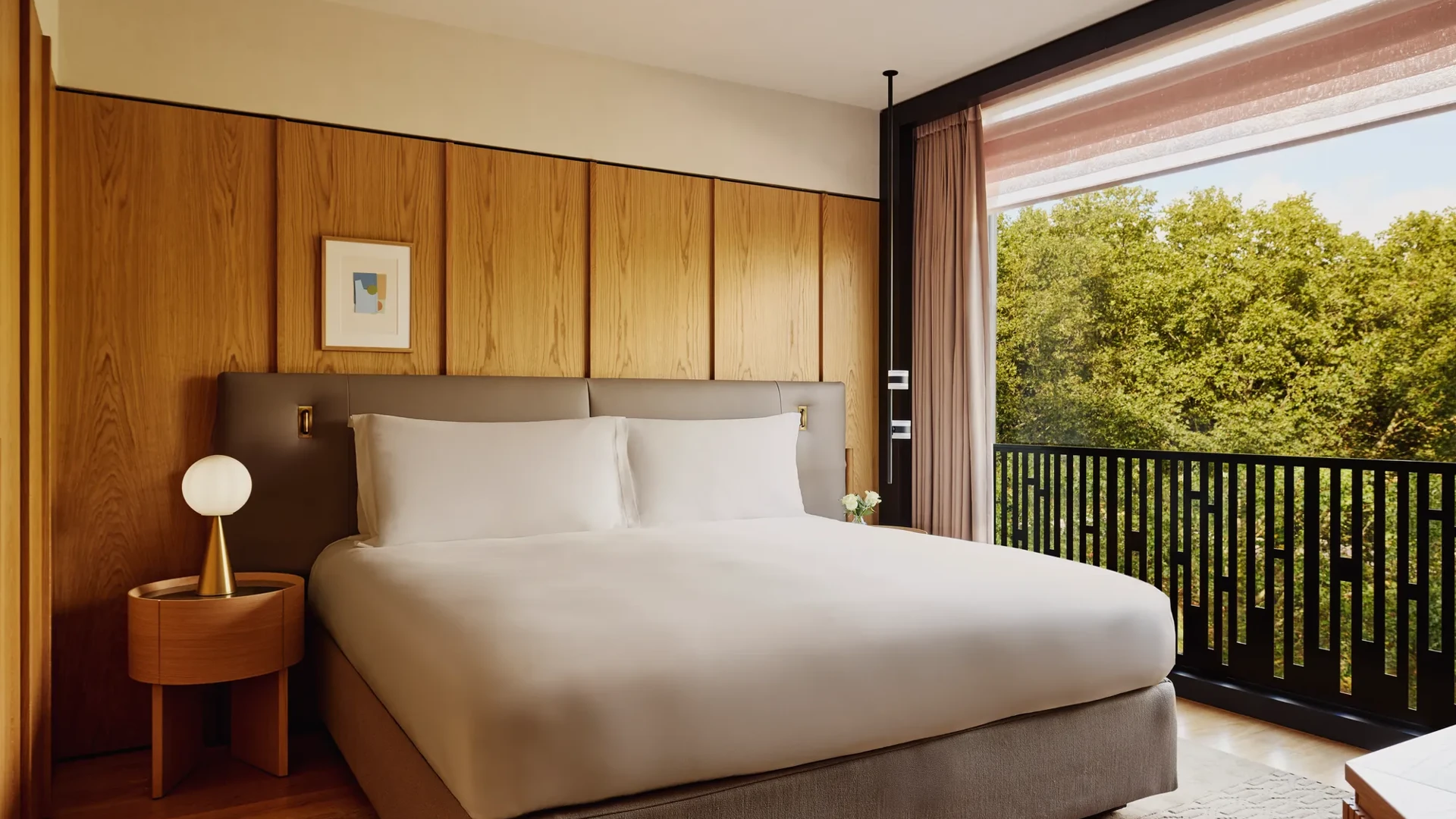 Hotel bedroom with king bed, bedside lamps, and city view through large window.