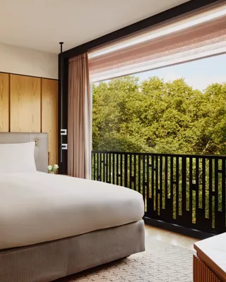 Hotel bedroom with king bed, bedside lamps, and city view through large window.