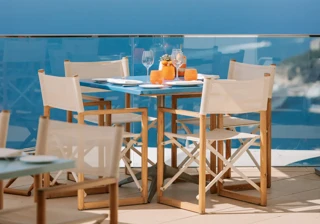 Table de repas en extérieur dressée avec des boissons sous un parasol blanc, offrant une vue panoramique sur la mer depuis une terrasse vitrée.