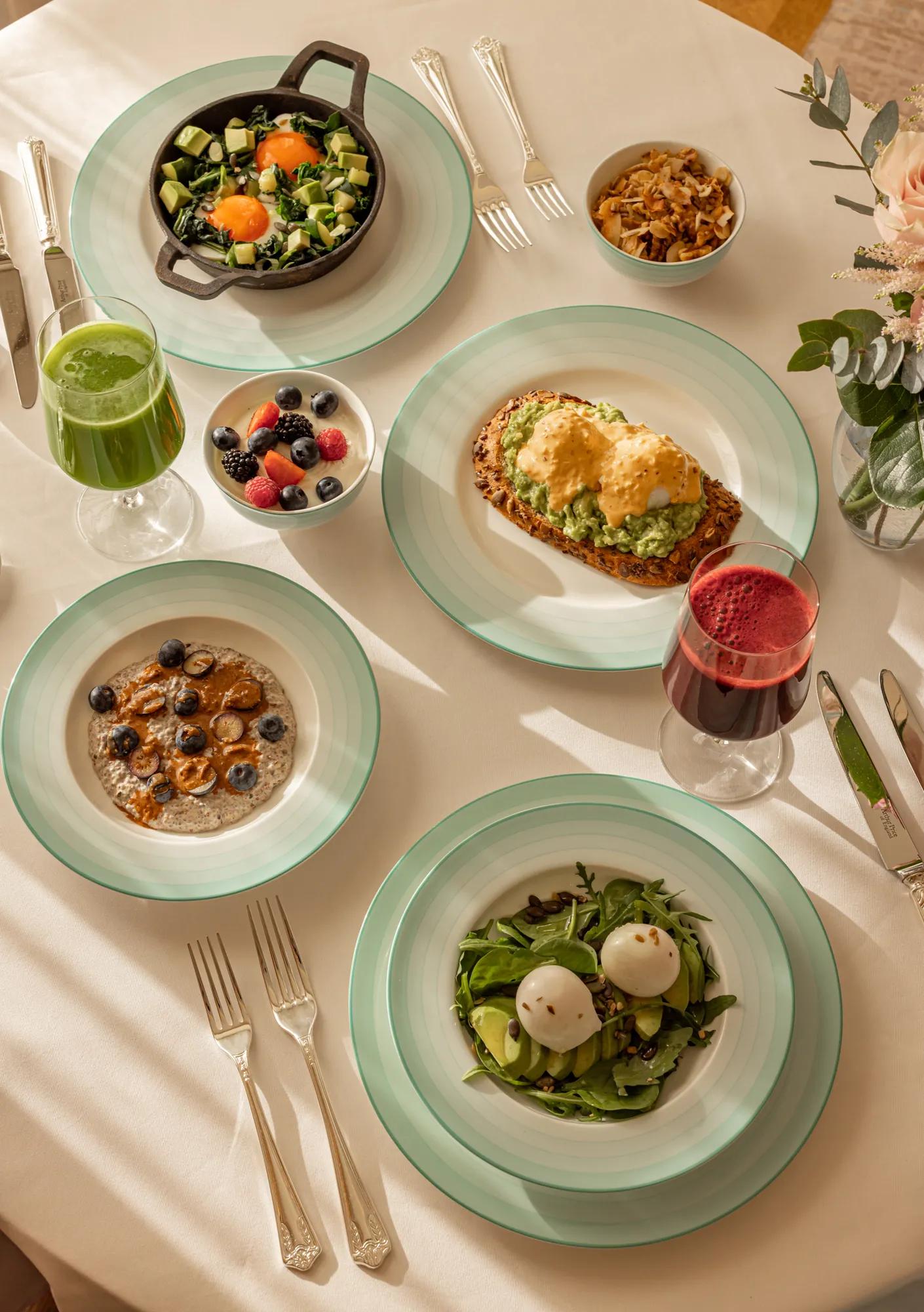 **Alt text (WCAG 2.2 AA):**
Breakfast table with avocado toast, baked eggs, porridge, burrata salad, fresh berries and green and berry juices in sunlight.
