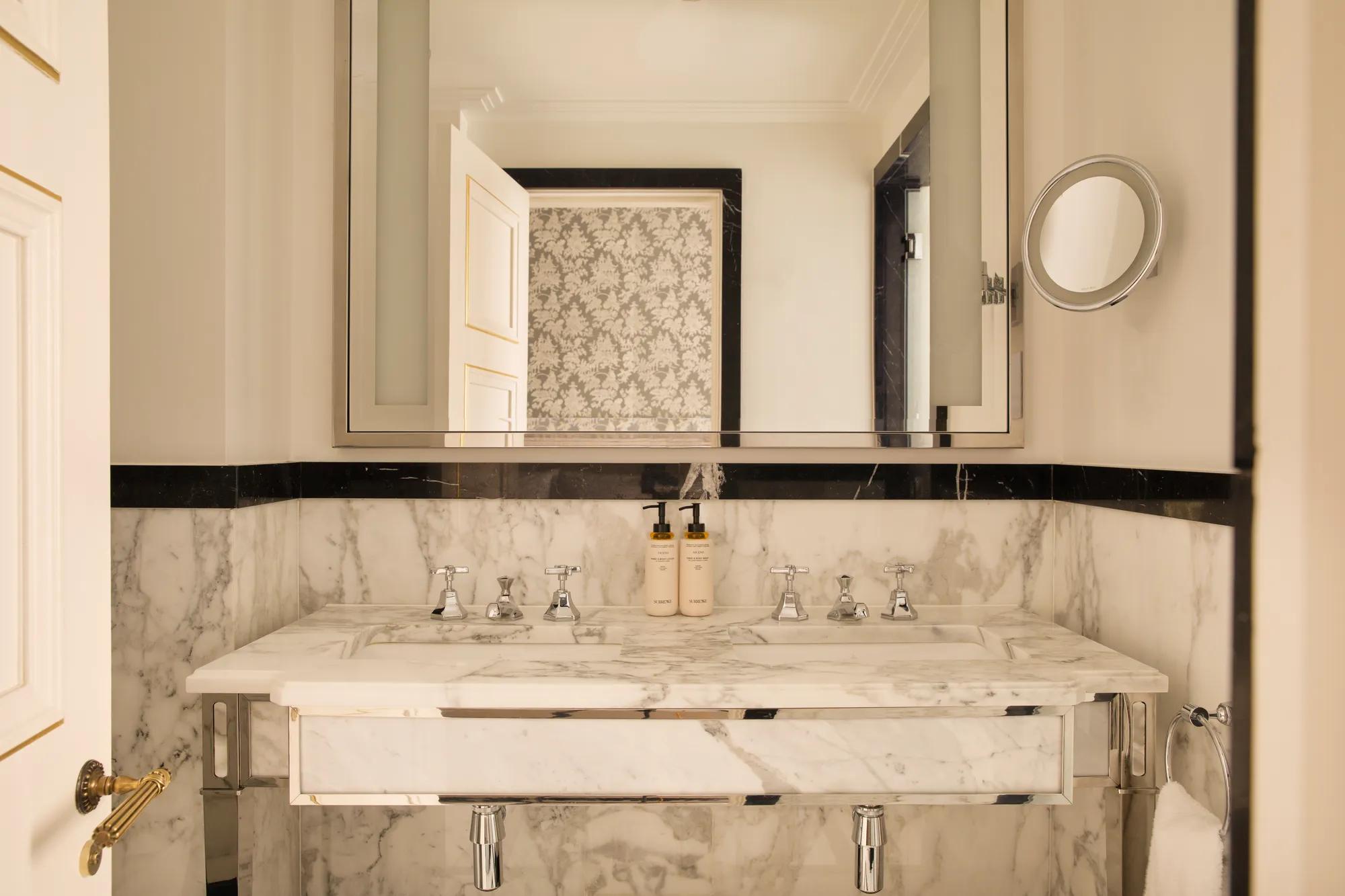 **Alt text (WCAG 2.2 AA, ≤125 characters):**

Marble bathroom with a double vanity, large illuminated mirror, luxury toiletries and polished chrome fittings.
