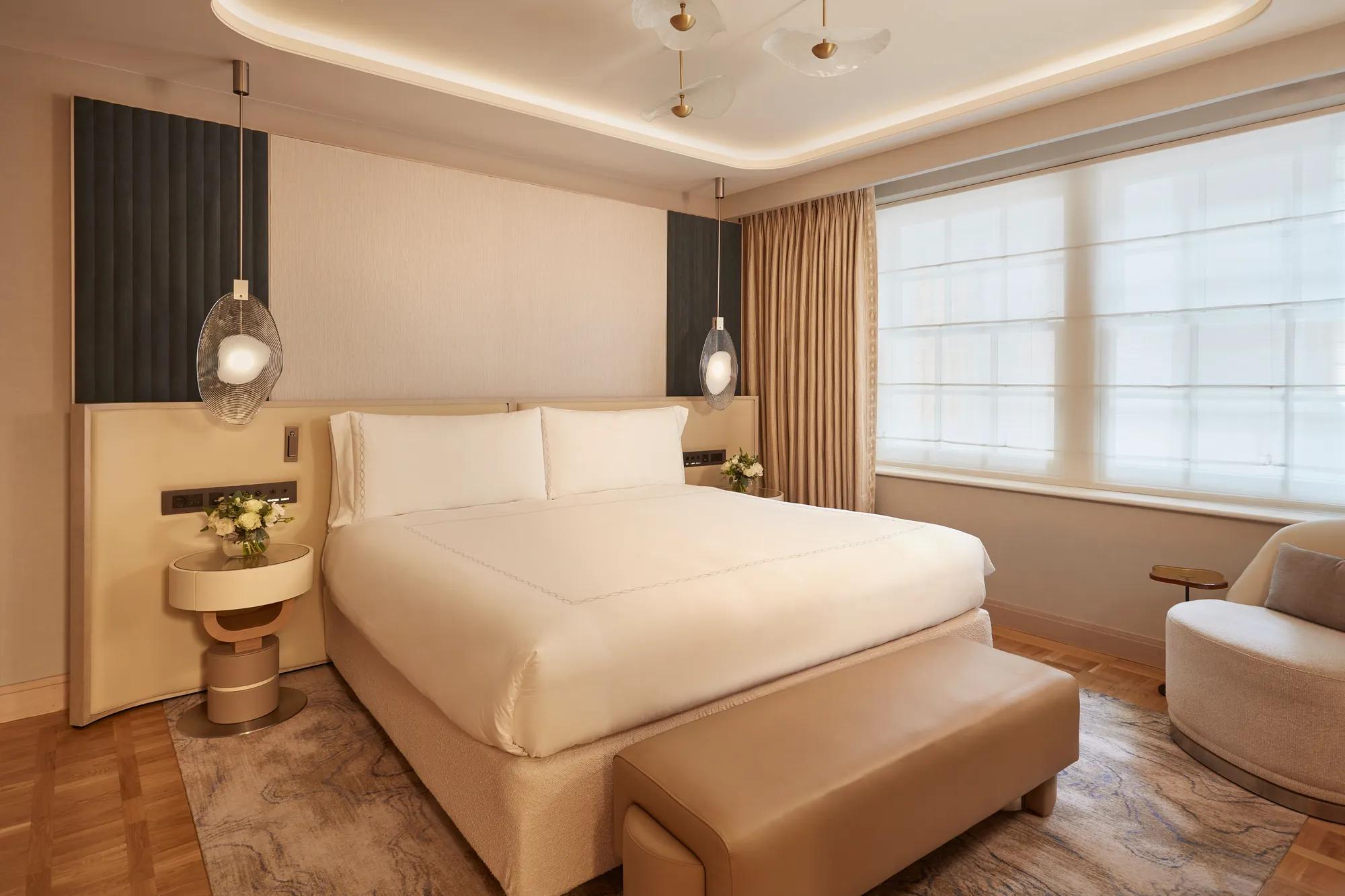 Contemporary bedroom featuring a large bed with cream bedding, pendant bedside lights, and warm neutral tones with modern furnishings.