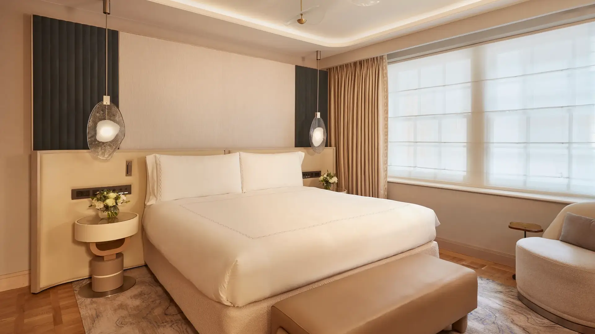 Contemporary bedroom featuring a large bed with cream bedding, pendant bedside lights, and warm neutral tones with modern furnishings.