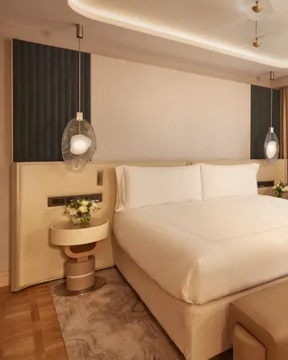Contemporary bedroom featuring a large bed with cream bedding, pendant bedside lights, and warm neutral tones with modern furnishings.