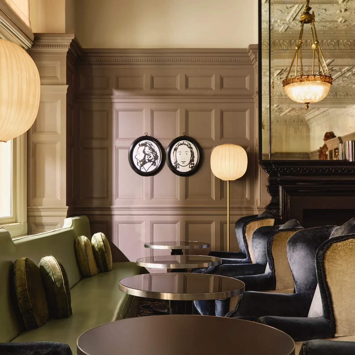 Elegant lounge seating with velvet chairs, round tables, and paneled walls decorated with framed portraits and warm lighting.