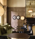 Elegant lounge seating with velvet chairs, round tables, and paneled walls decorated with framed portraits and warm lighting.