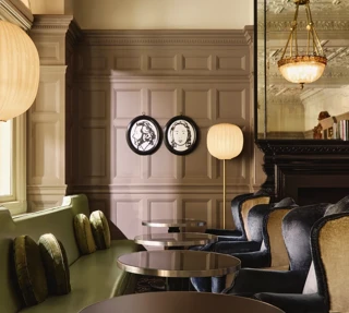 Elegant lounge seating with velvet chairs, round tables, and paneled walls decorated with framed portraits and warm lighting.