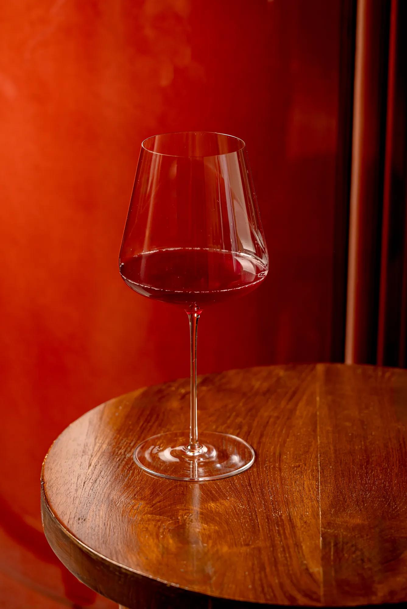 Glass of red wine on a round wooden table against a warm red background.
