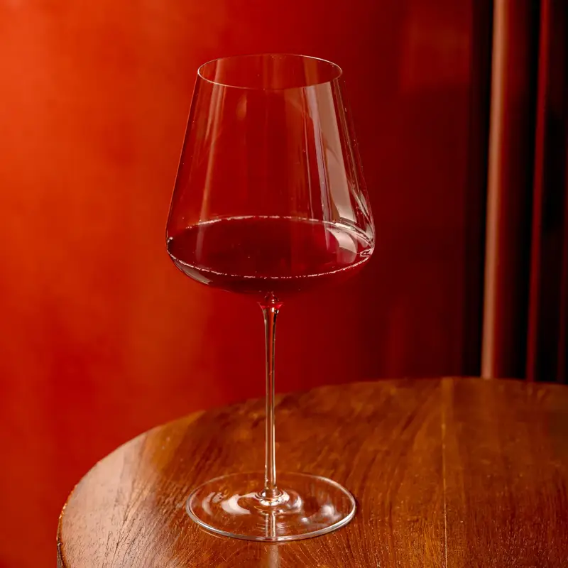 Glass of red wine on a round wooden table against a warm red background.