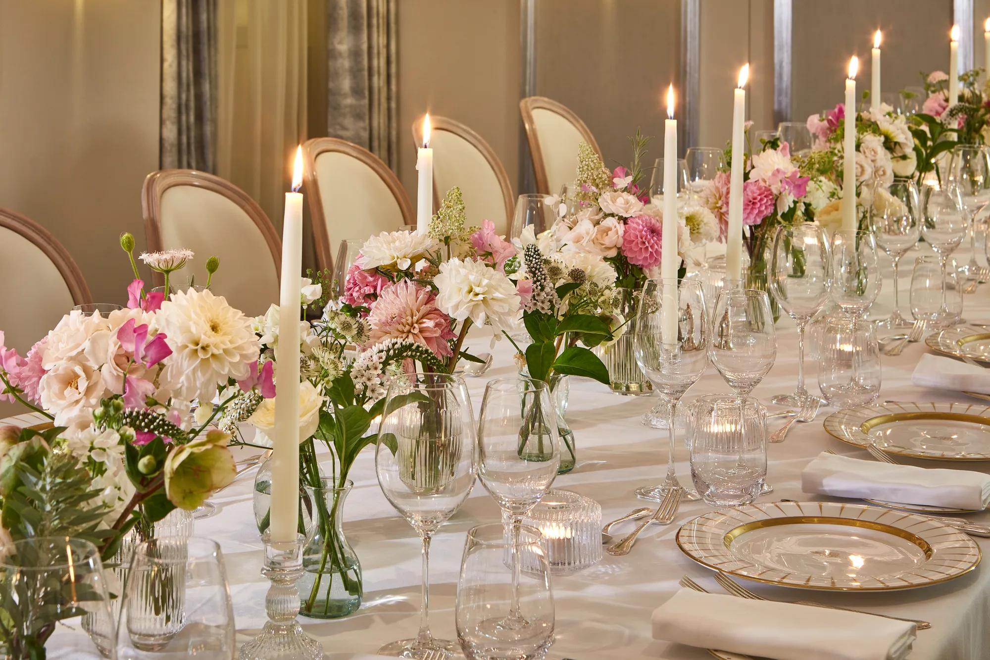 Elegant banquet table with pink floral arrangements, tall candles, crystal glassware, and gold-rimmed place settings.