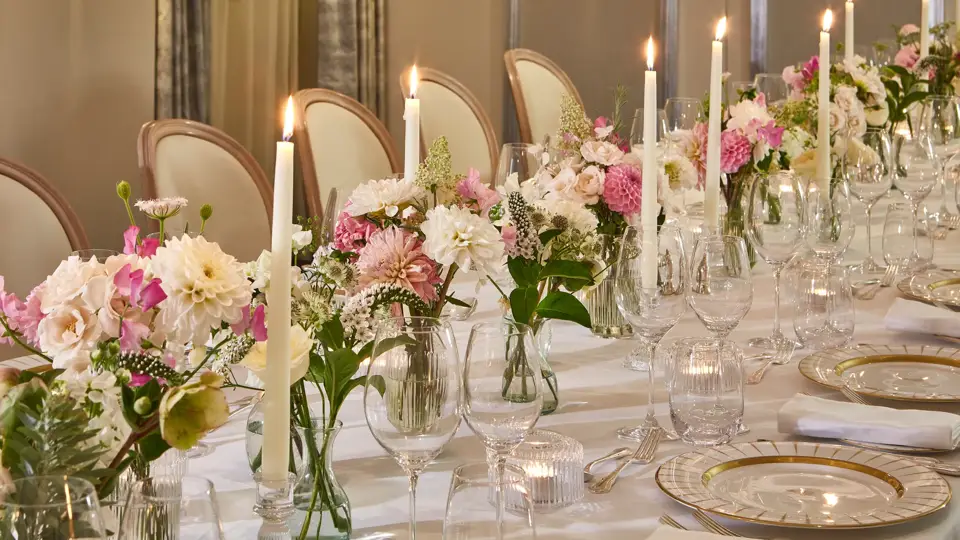 Elegant banquet table with pink floral arrangements, tall candles, crystal glassware, and gold-rimmed place settings.