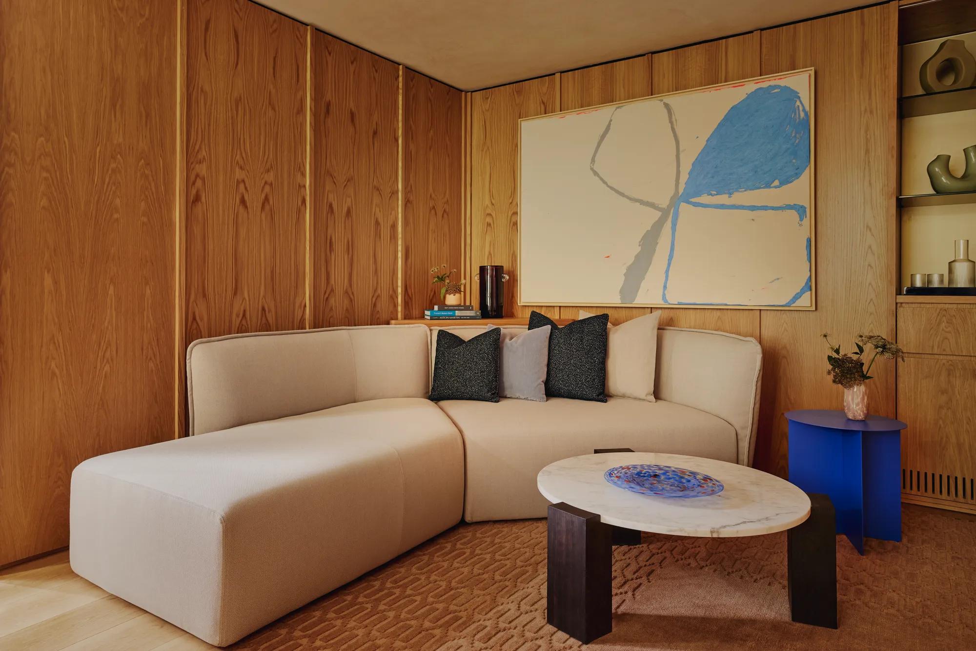 Cosy corner lounge with off-white L-shaped sofa, large abstract artwork, and marble coffee table with cobalt side table.