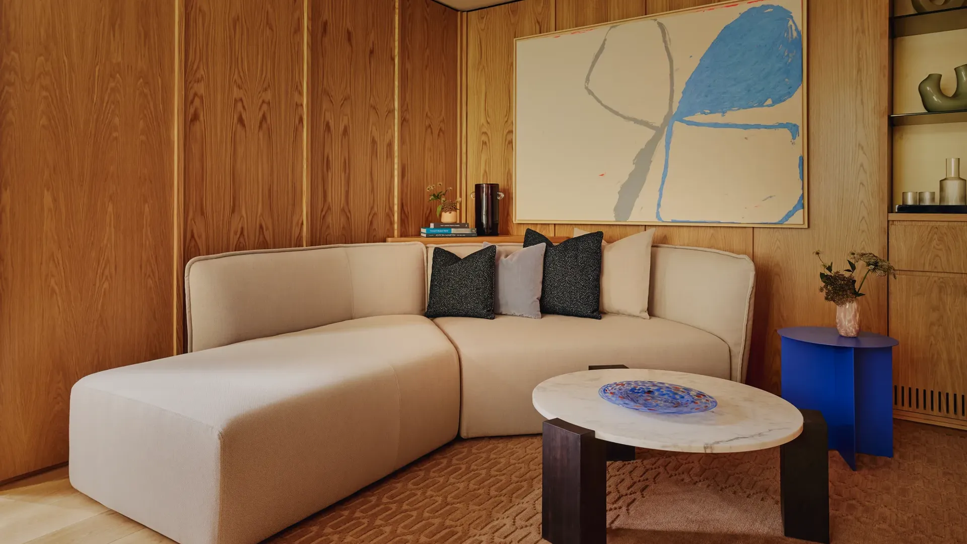 Cosy corner lounge with off-white L-shaped sofa, large abstract artwork, and marble coffee table with cobalt side table.