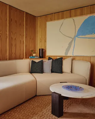 Cosy corner lounge with off-white L-shaped sofa, large abstract artwork, and marble coffee table with cobalt side table.