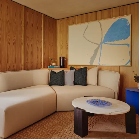 Cosy corner lounge with off-white L-shaped sofa, large abstract artwork, and marble coffee table with cobalt side table.