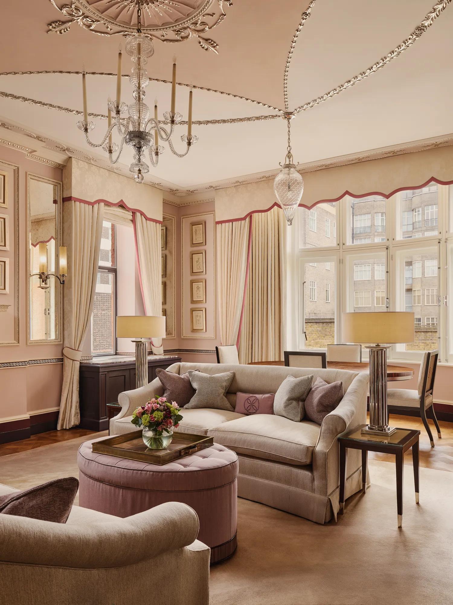 Elegant living room with cream sofas, pink accents, chandelier, and large windows framing courtyard views.