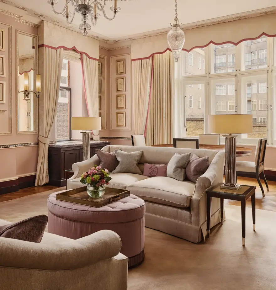 Elegant living room with cream sofas, pink accents, chandelier, and large windows framing courtyard views.