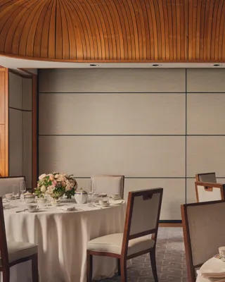Intimate event room with round tables, floral centerpieces, fine china, and wood-panel ceiling under soft natural light.