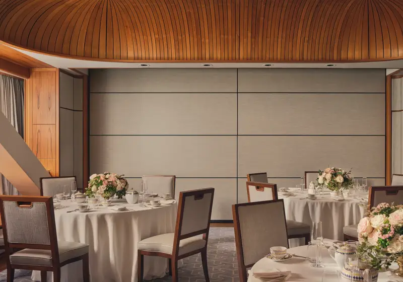 Intimate event room with round tables, floral centerpieces, fine china, and wood-panel ceiling under soft natural light.