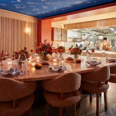 Candlelit chef’s table set with flowers beside an open kitchen where chefs prepare dishes.