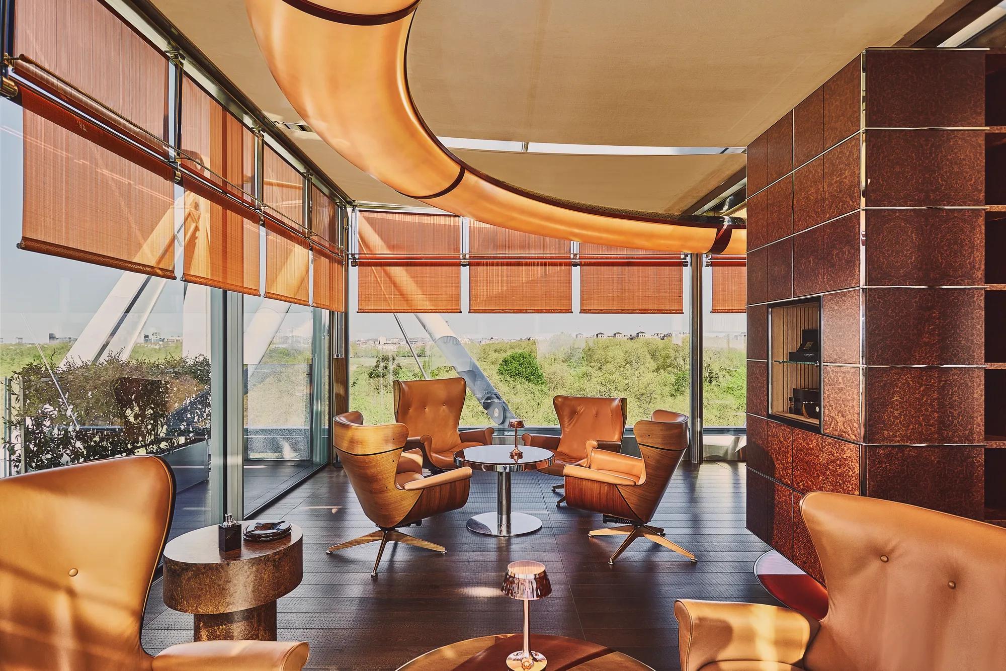 Rooftop lounge with leather armchairs, copper fireplace, and sweeping green views through floor-to-ceiling windows.