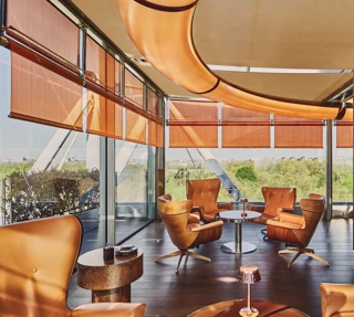 Rooftop lounge with leather armchairs, copper fireplace, and sweeping green views through floor-to-ceiling windows.