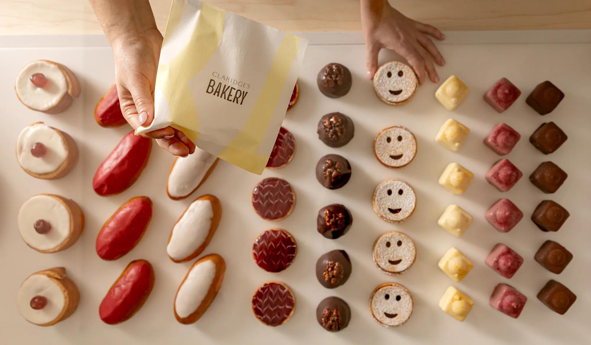 Hand holding a Claridge’s Bakery bag above a neatly arranged selection of colourful pastries.