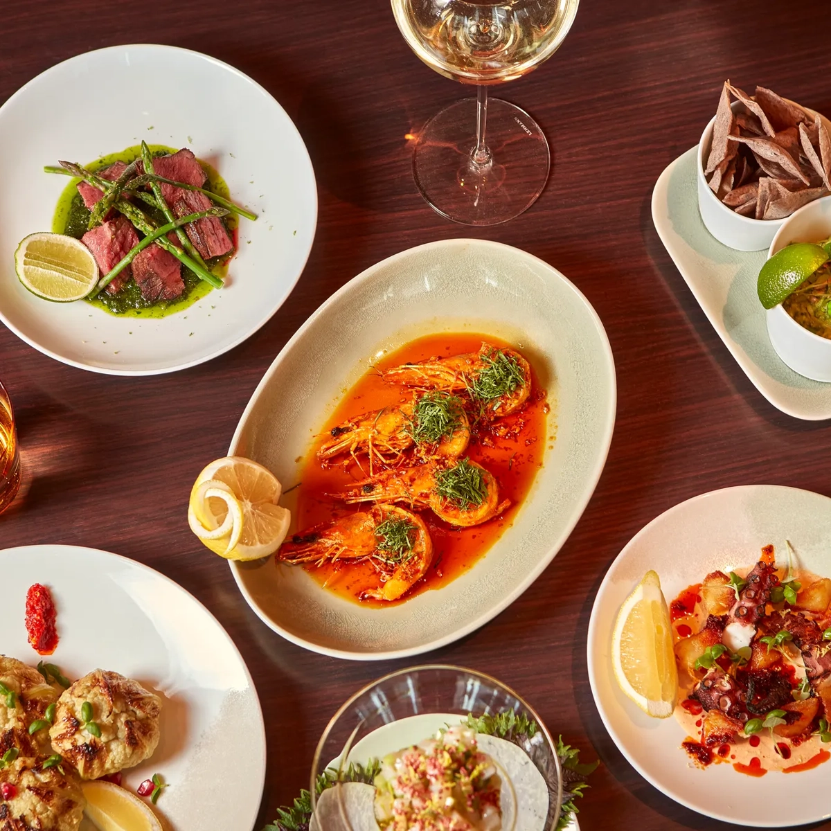Overhead view of assorted seafood dishes on a wooden table, including prawns, tuna, ceviche, small plates, and drinks.