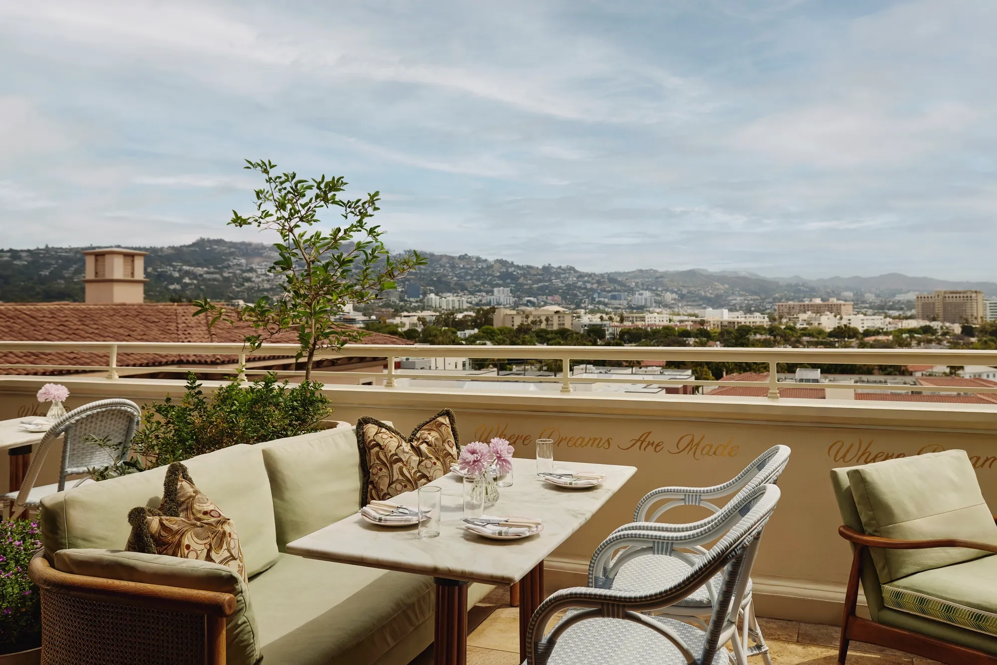Al fresco lounge on the rooftop at Dante Beverly Hills with marble tables, green cushions, and city skyline views above “Where Dreams Are Made.”