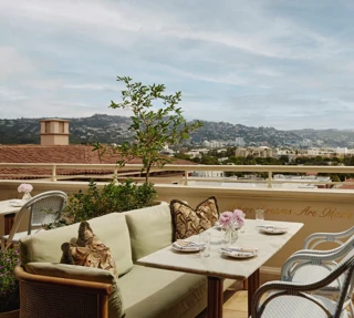 Al fresco lounge on the rooftop at Dante Beverly Hills with marble tables, green cushions, and city skyline views above “Where Dreams Are Made.”