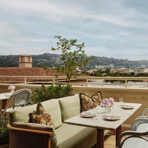 Al fresco lounge on the rooftop at Dante Beverly Hills with marble tables, green cushions, and city skyline views above “Where Dreams Are Made.”